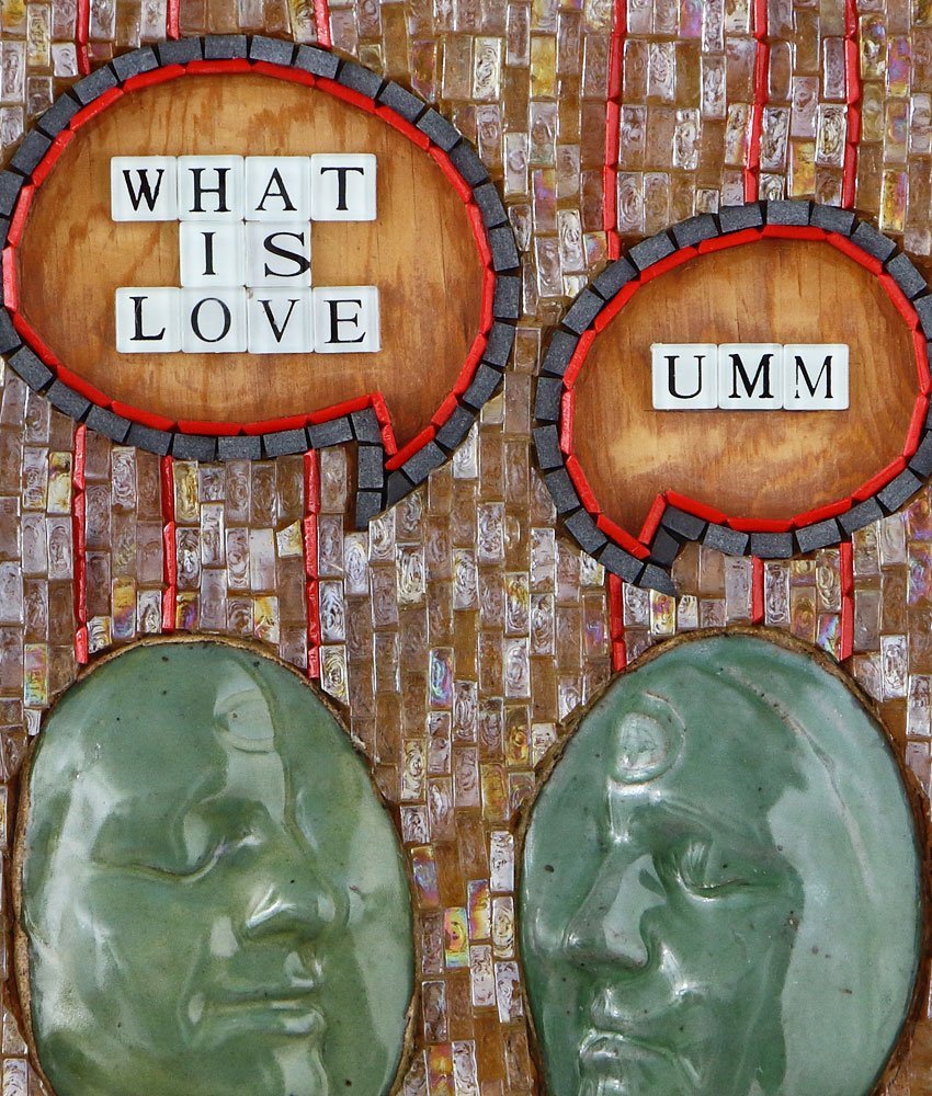 Close up detail of Caryn Mitchell’s, What is Love?, 16 x 20, mixed media wall art design made with two life-casted stoneware teal green facial profiles with talk bubbles with scrabble letters above their heads clear mosaic glass, Sicis red smalto. The left talk bubble asks, “What is love?” with the right talk bubble responding, “UMMM.”